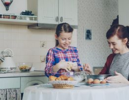 Little cute girl helping her mother in the kitchen stirring dough for cookies into bowl. Family, food, home and people concept