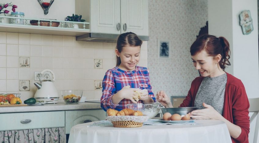 Little cute girl helping her mother in the kitchen stirring dough for cookies into bowl. Family, food, home and people concept